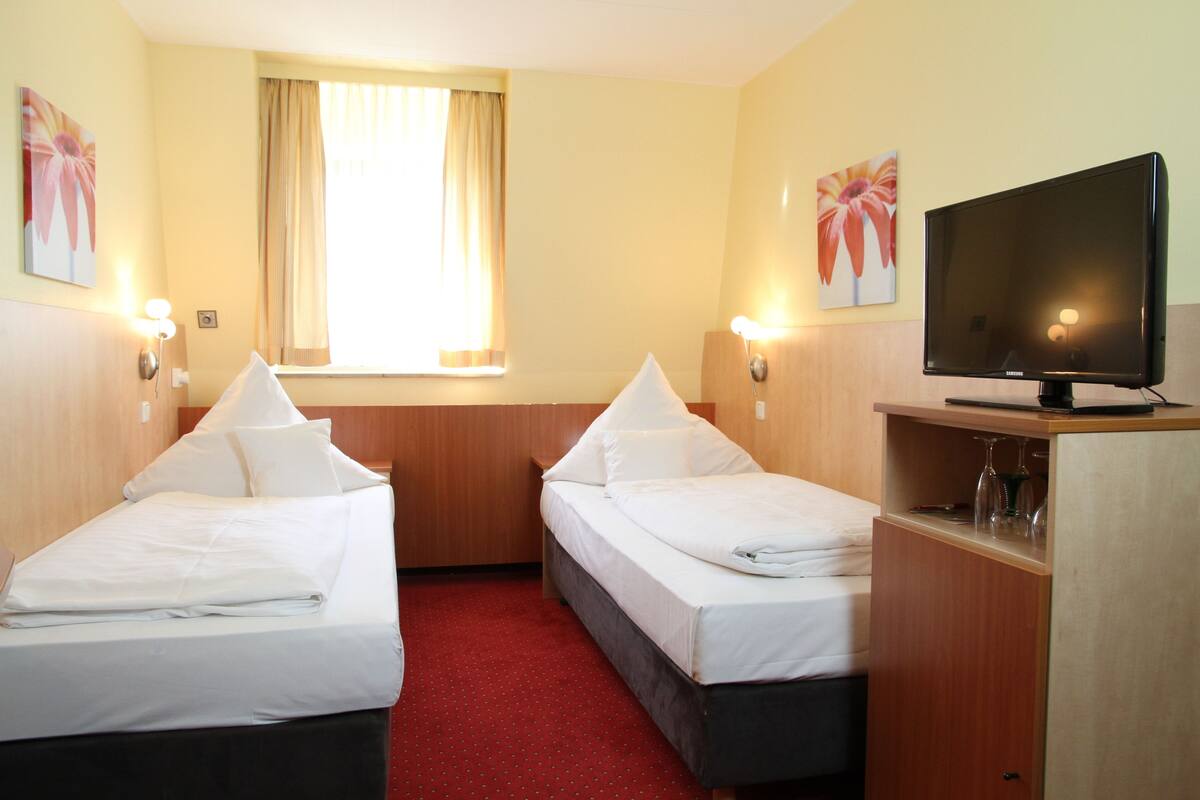 A hotel room with two beds, a television, and a window with curtains.