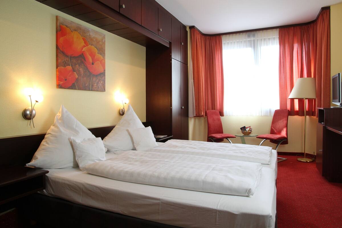 A hotel room with a double bed, two bedside tables, a desk with a chair, a TV, and a painting on the wall.