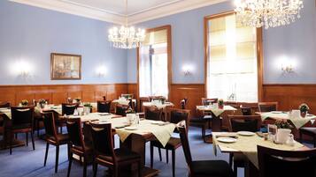 Un comedor formal con varias mesas, sillas, candelabros y apliques de pared.