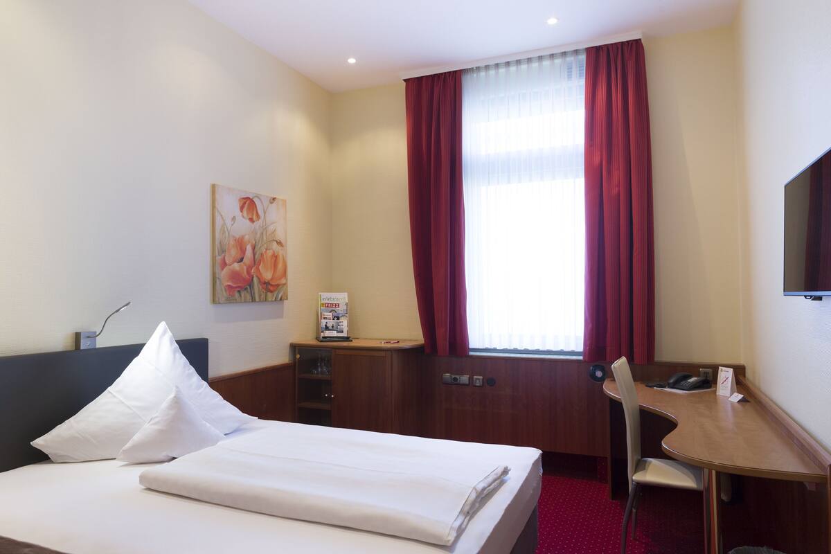 A hotel room with a bed, a desk, a chair, a television, and a window with curtains.
