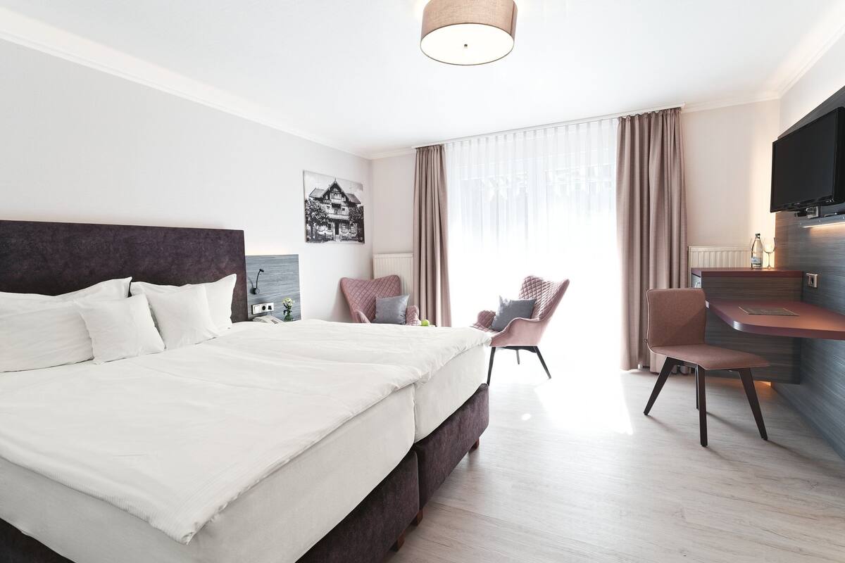 A modern hotel room with a large bed, a desk, a chair, and a TV.