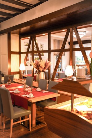 A dining area with wooden beams, red tablecloths, and modern chairs.