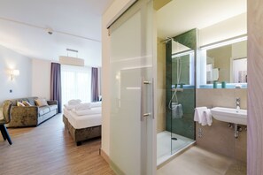 A hotel room with a bed, a sofa, a glass-enclosed shower, and a bathroom with a sink and mirror.