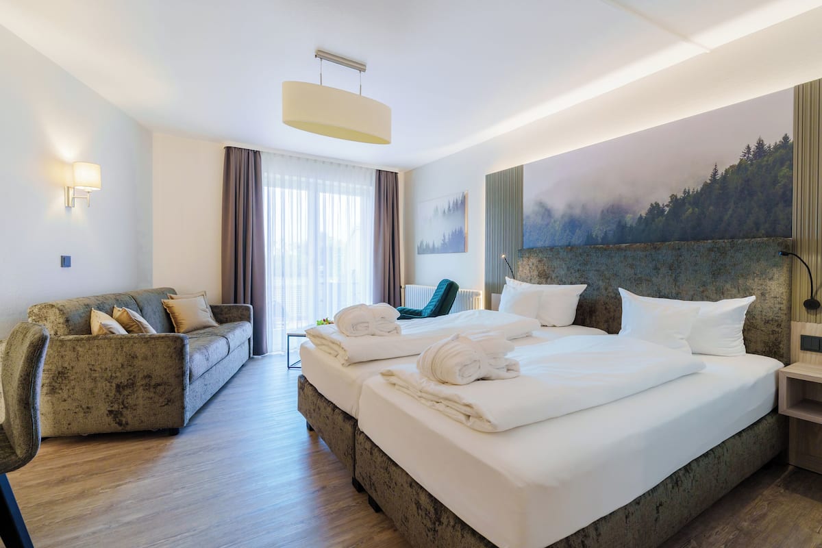 A hotel room with a bed, a sofa, a chair, and a painting on the wall.