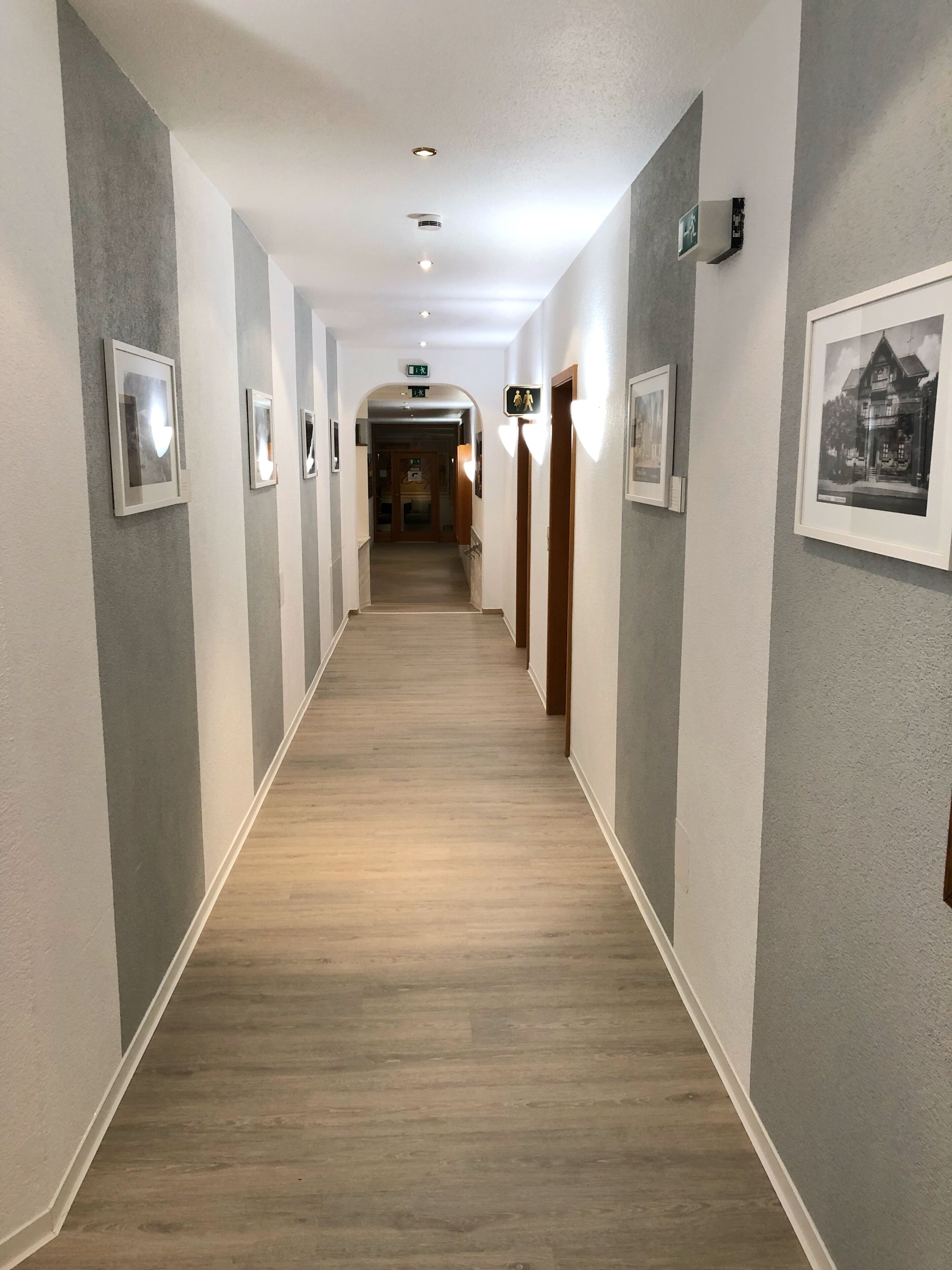 Ein Hotelgang mit gerahmten Bildern an den Wänden, Holzboden und einem Ausgangsschild.