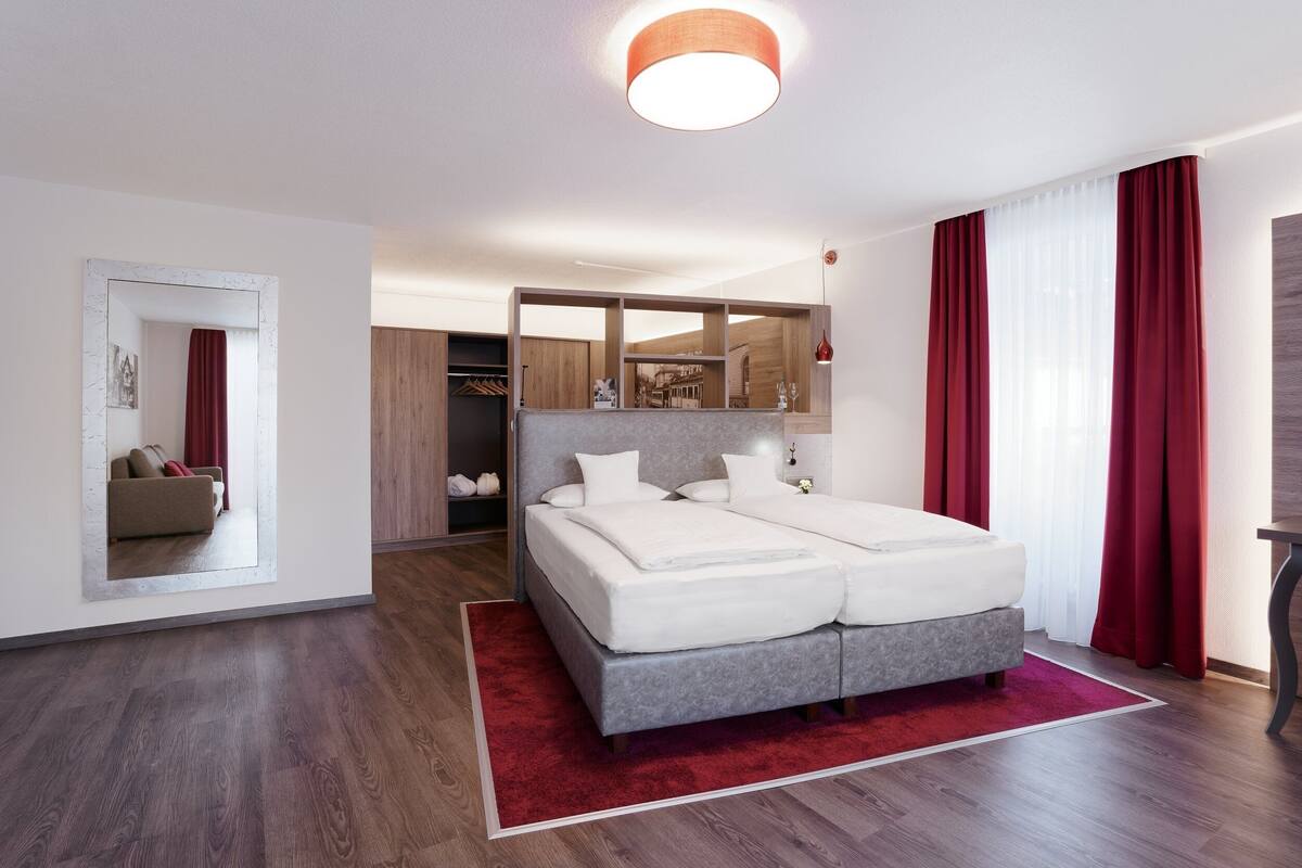 A modern bedroom with a double bed, a red rug, and a wooden floor.