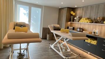 A medical examination room with two examination tables, a wooden cabinet with towels, and a window with curtains.