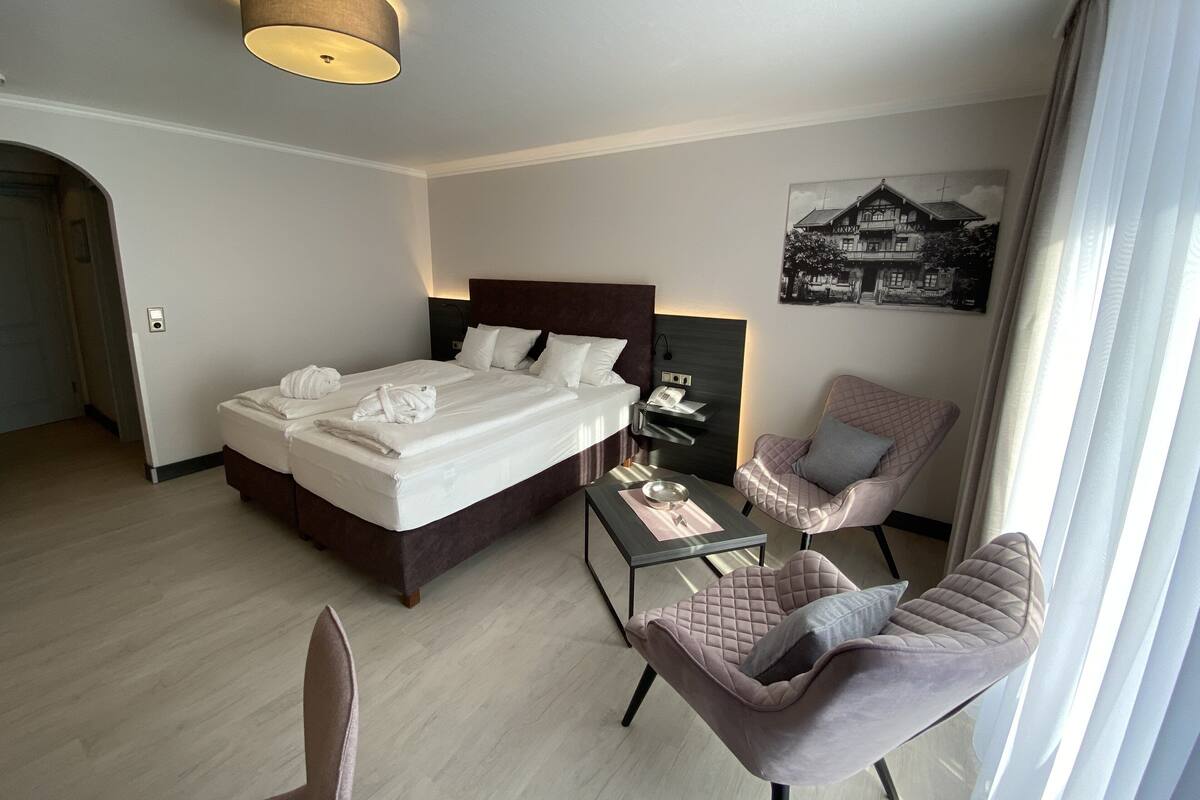 A hotel room with a bed, a chair, a table, and a wall-mounted phone.