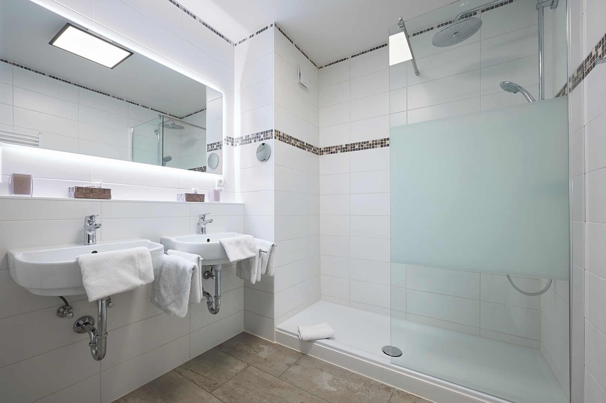 Un baño moderno con dos lavamanos, cabina de ducha con mampara de cristal y un espejo sobre los lavamanos.