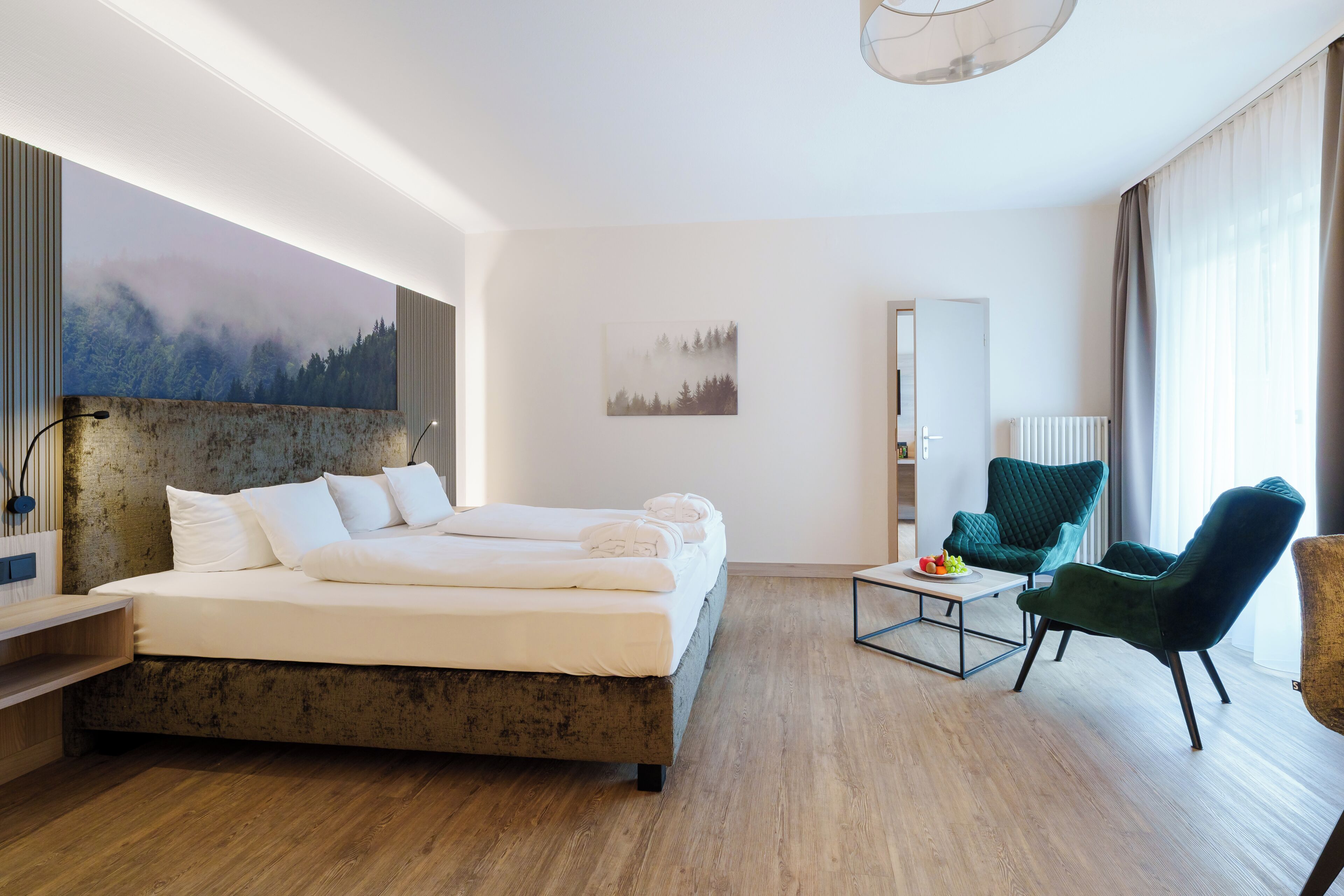 A modern hotel room with a large bed, two chairs, a small table, and artwork on the walls.