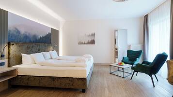 A modern hotel room with a large bed, two chairs, a small table, and artwork on the walls.