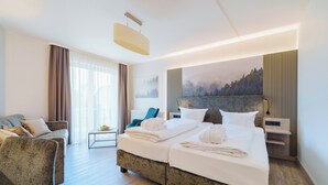 A hotel room with a bed, a sofa, a coffee table, and a view of a forest through the window. -  Hotel Ritter Badenweiler (Badenweiler)