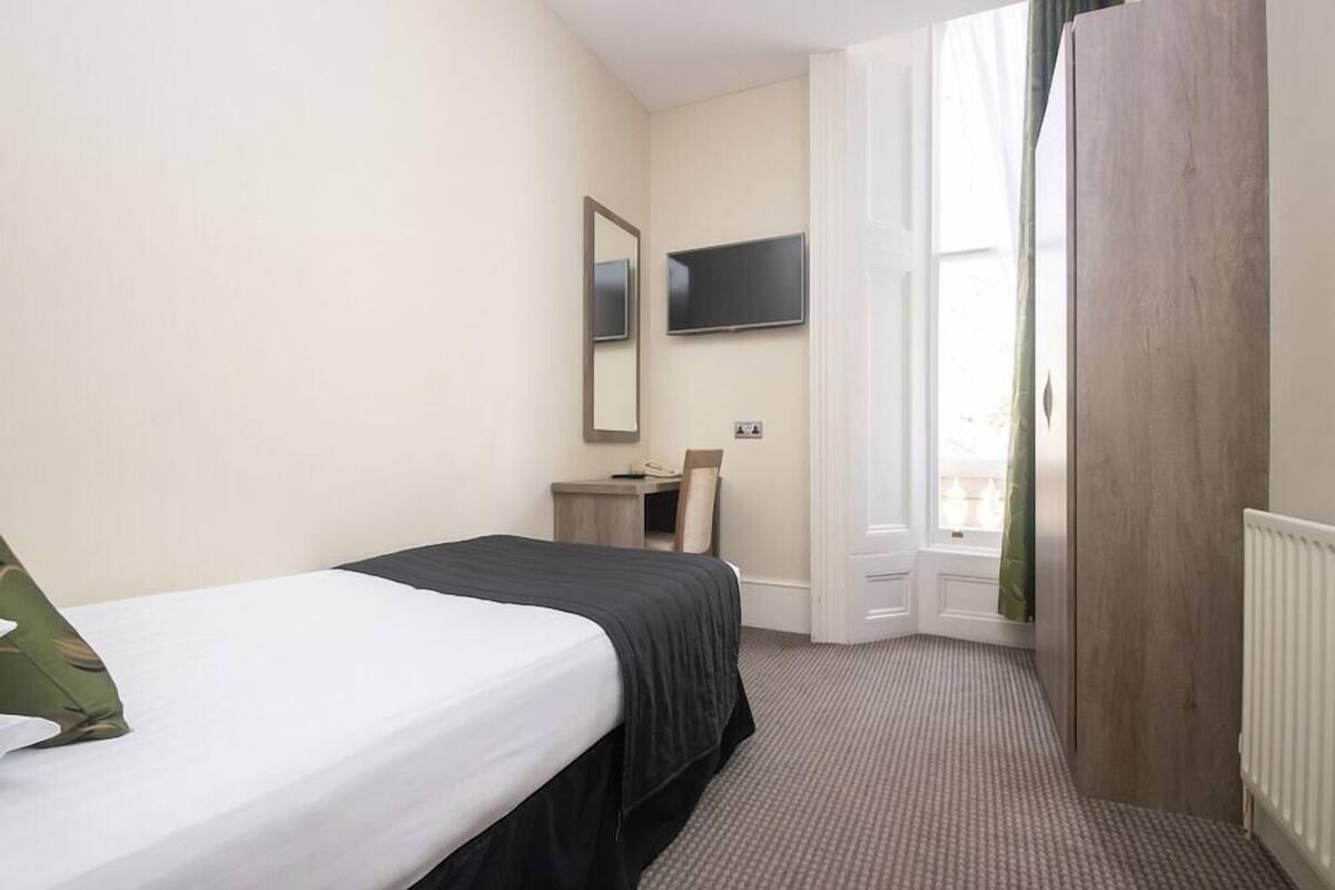 Una habitación de hotel con cama, escritorio, silla, televisor y ventana con cortinas.