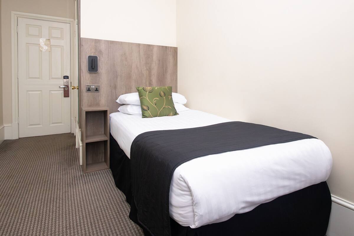 Una habitación de hotel con cama, puerta, interruptor de luz y panel de control montado en la pared.