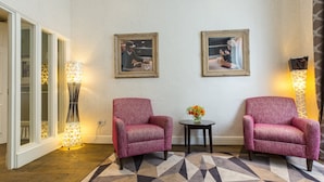 A room with two armchairs, a small table with a vase of flowers, and two framed pictures on the wall. - Kensington Gardens Hotel (London)