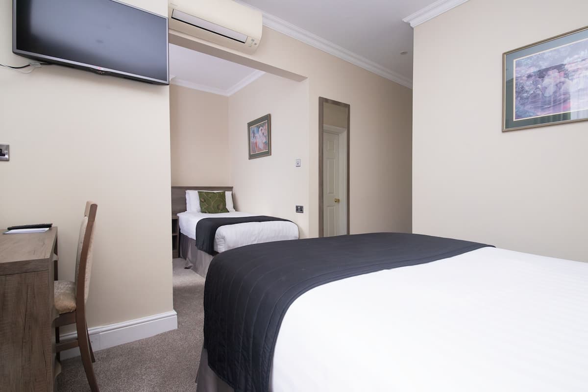 Habitación de hotel con una cama grande, un escritorio, una silla, un televisor y una puerta que da a otra habitación.