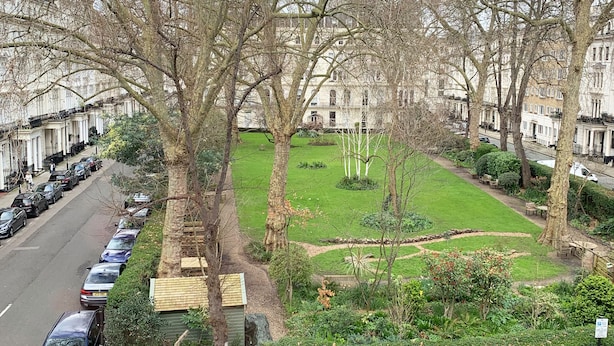 A residential street with parked cars and a well-maintained lawn with trees and shrubs. - Kensington Gardens Hotel (London)