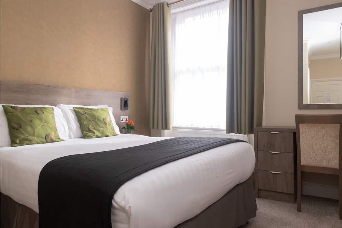 Habitación de hotel con una cama grande, una mesita de noche, un espejo y una ventana con cortinas.