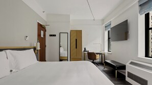 A hotel room with a large bed, a desk, a chair, a wardrobe, and a TV mounted on the wall.