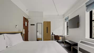 Ein Hotelzimmer mit einem großen Bett, einem Schreibtisch, einem Stuhl, einem Kleiderschrank und einem an der Wand befestigten Fernseher.