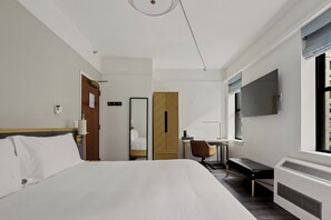 A hotel room with a large bed, a desk, a chair, a wardrobe, and a TV mounted on the wall.