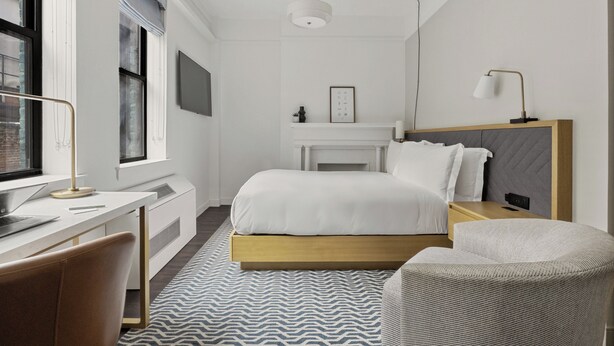 A modern bedroom with a bed, bedside table, lamp, and a desk with a chair.