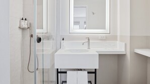 A modern bathroom with a glass-enclosed shower, a large mirror, and a white sink with a towel rack below.