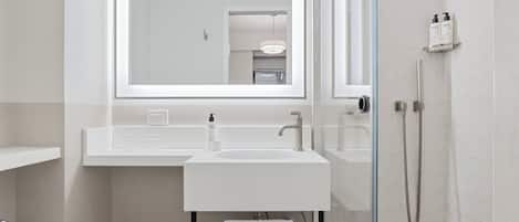Un baño moderno con cabina de ducha de vidrio, un lavabo blanco y un espejo grande sobre el lavabo.