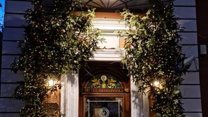 L’entrée d’un hôtel, avec une façade sombre, une porte en bois et une enseigne indiquant « HÔTEL DEI CONSOLI ».