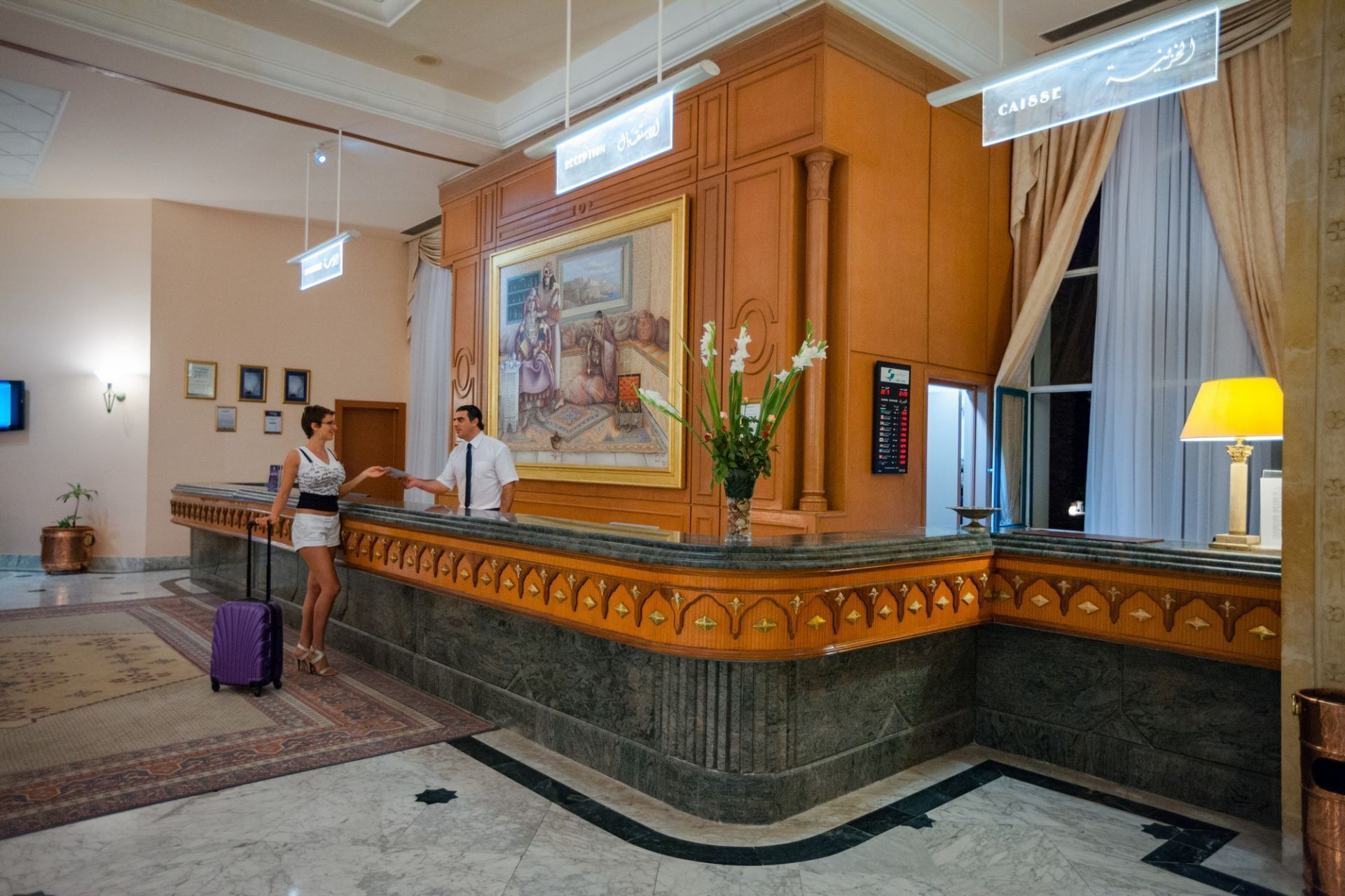 A reception area with a marble counter, a large painting, and a reception desk.