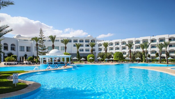 A large swimming pool with a gazebo, palm trees, and a multi-story hotel building in the background. - Mahdia Palace Thalasso (Mahdia)