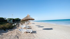 A beach with white lounge chairs and a thatched umbrella. - Mahdia Palace Thalasso (Mahdia)