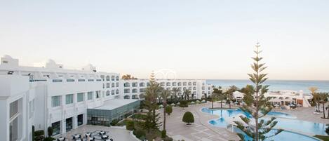 Un resort con varias edificaciones blancas, una piscina y vistas al mar.