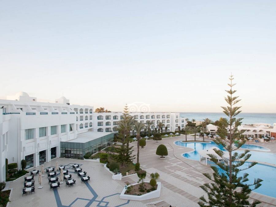 Un resort con varias edificaciones blancas, una piscina y vistas al mar.