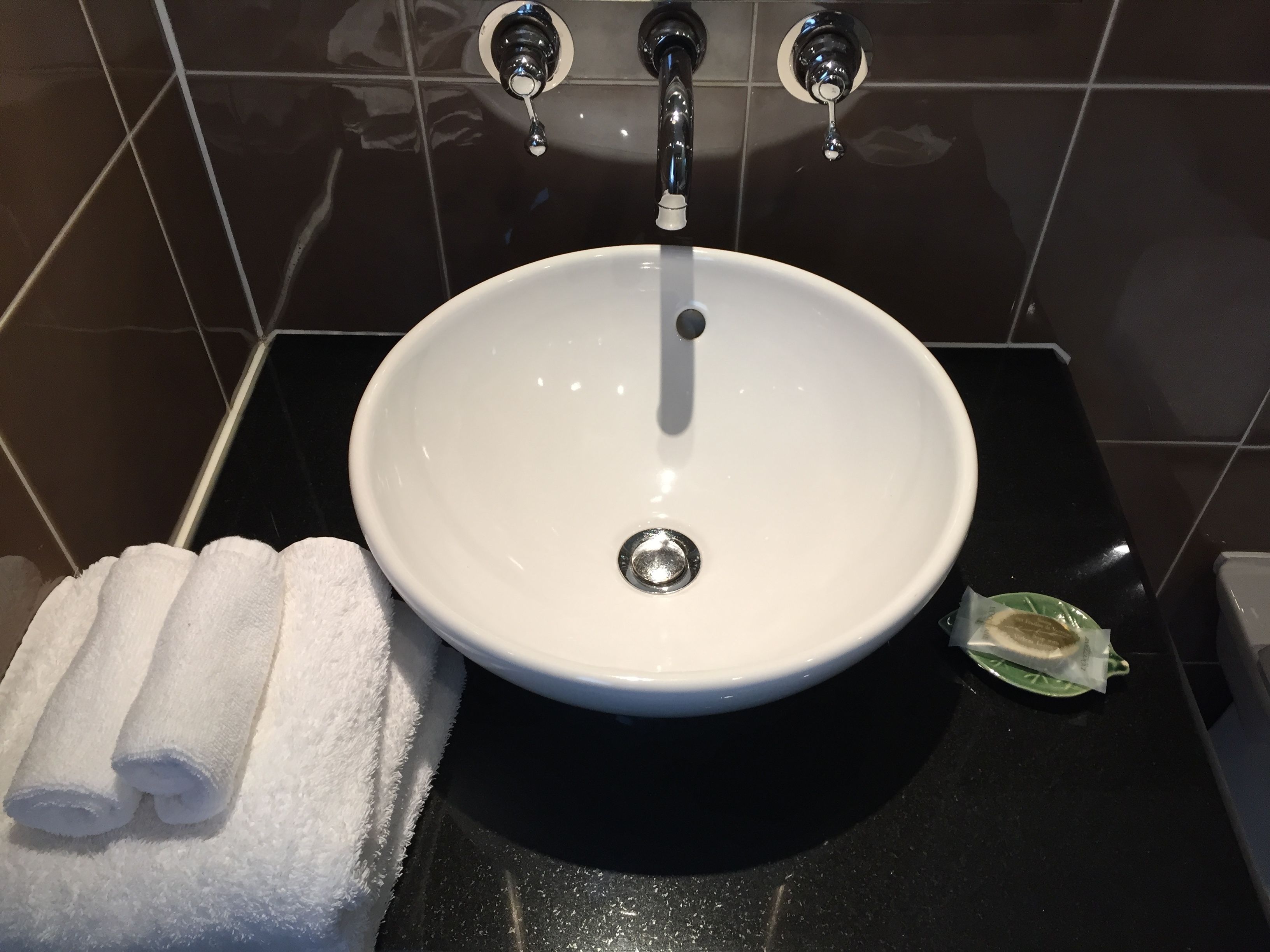 A bathroom with a white sink, black countertop, and a towel rack with folded towels.