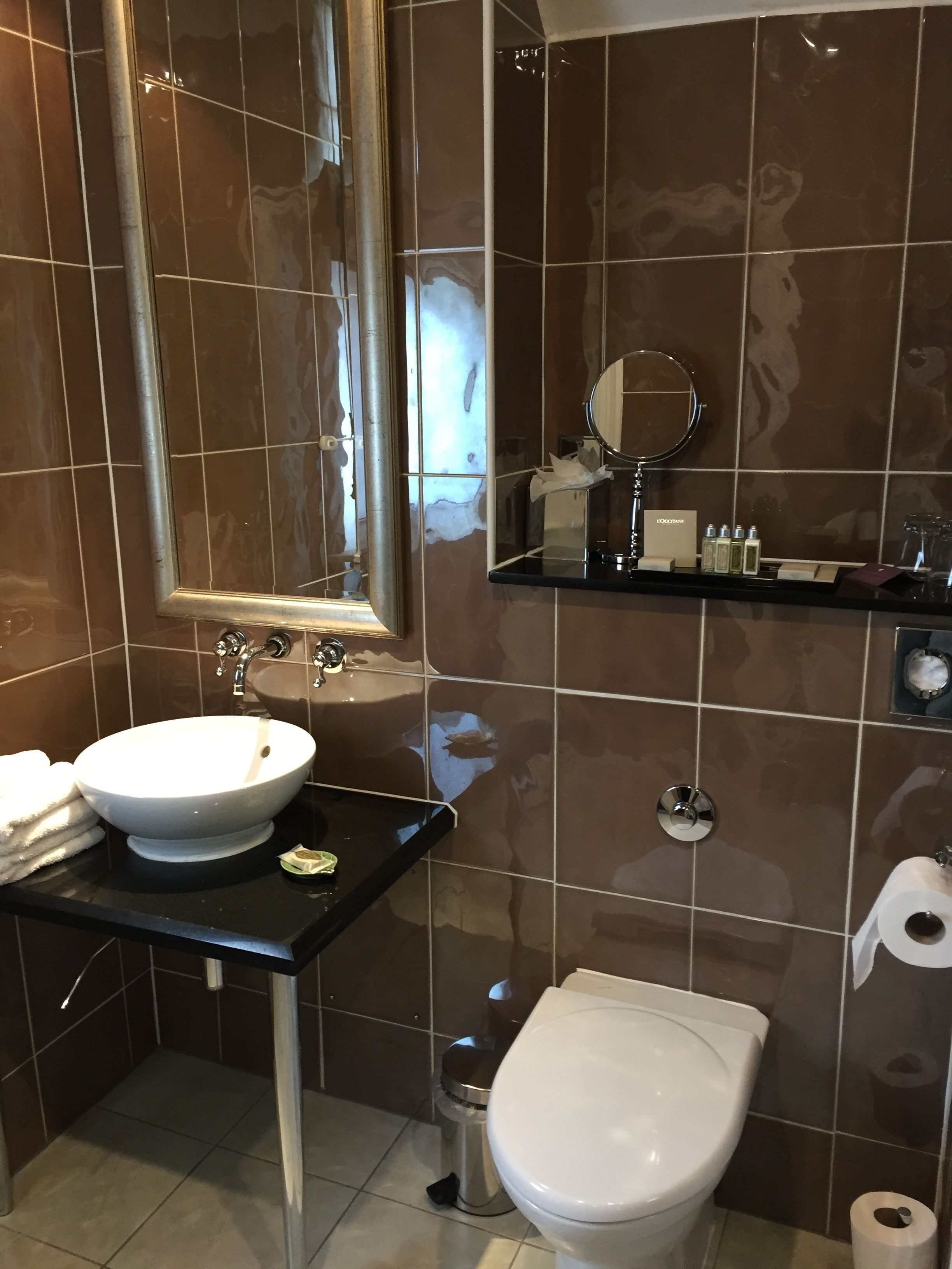 A modern bathroom with a white sink, a mirror, a toilet, and a shelf with toiletries.