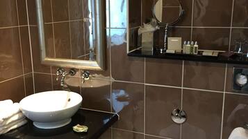 A modern bathroom with a white sink, a mirror, a toilet, and a shelf with toiletries.