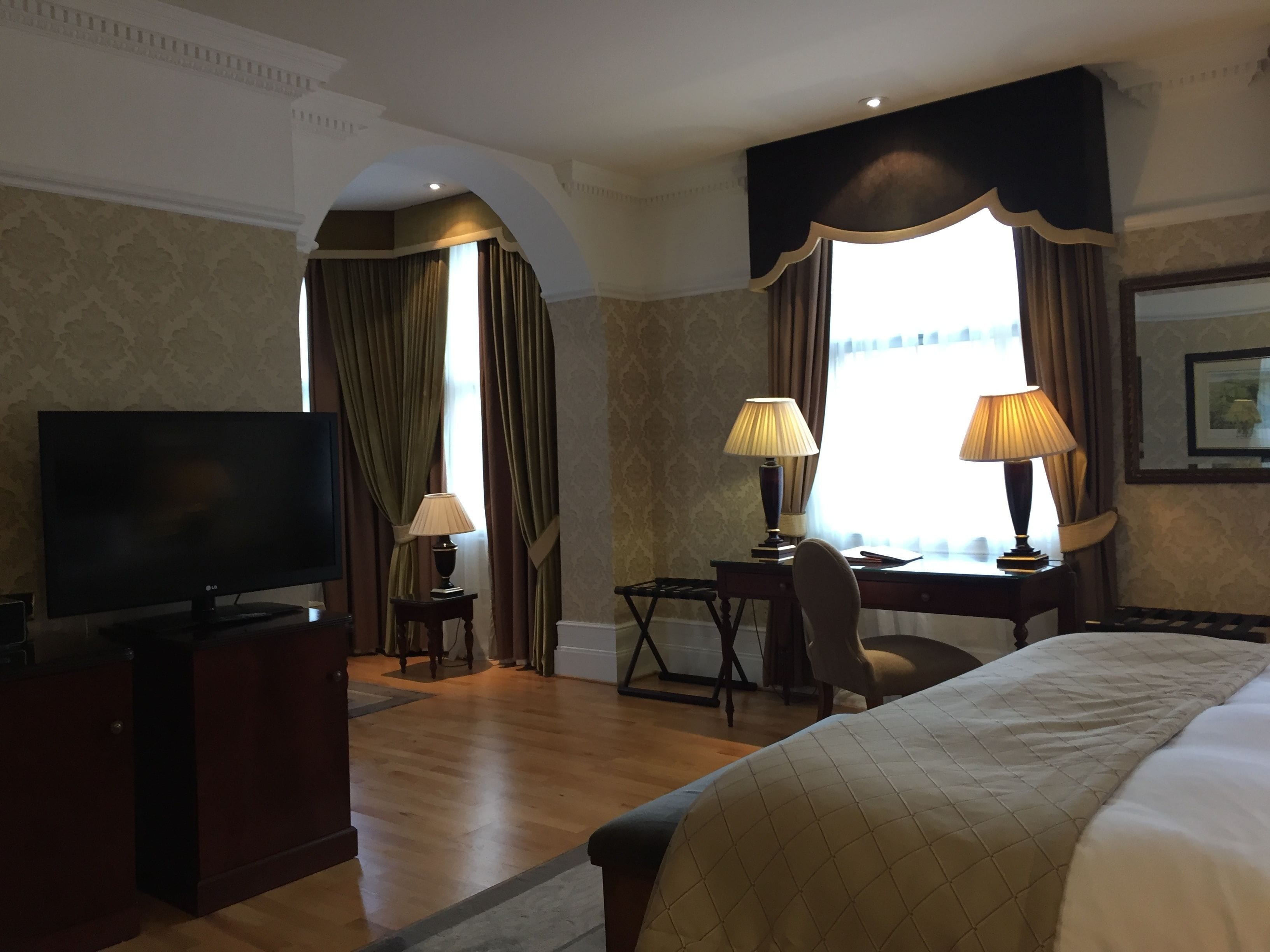 A hotel room with a bed, a desk with two lamps, a television, and a chair.