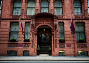 A red brick building with ornate architectural details, a central entrance with a canopy, and two flags.