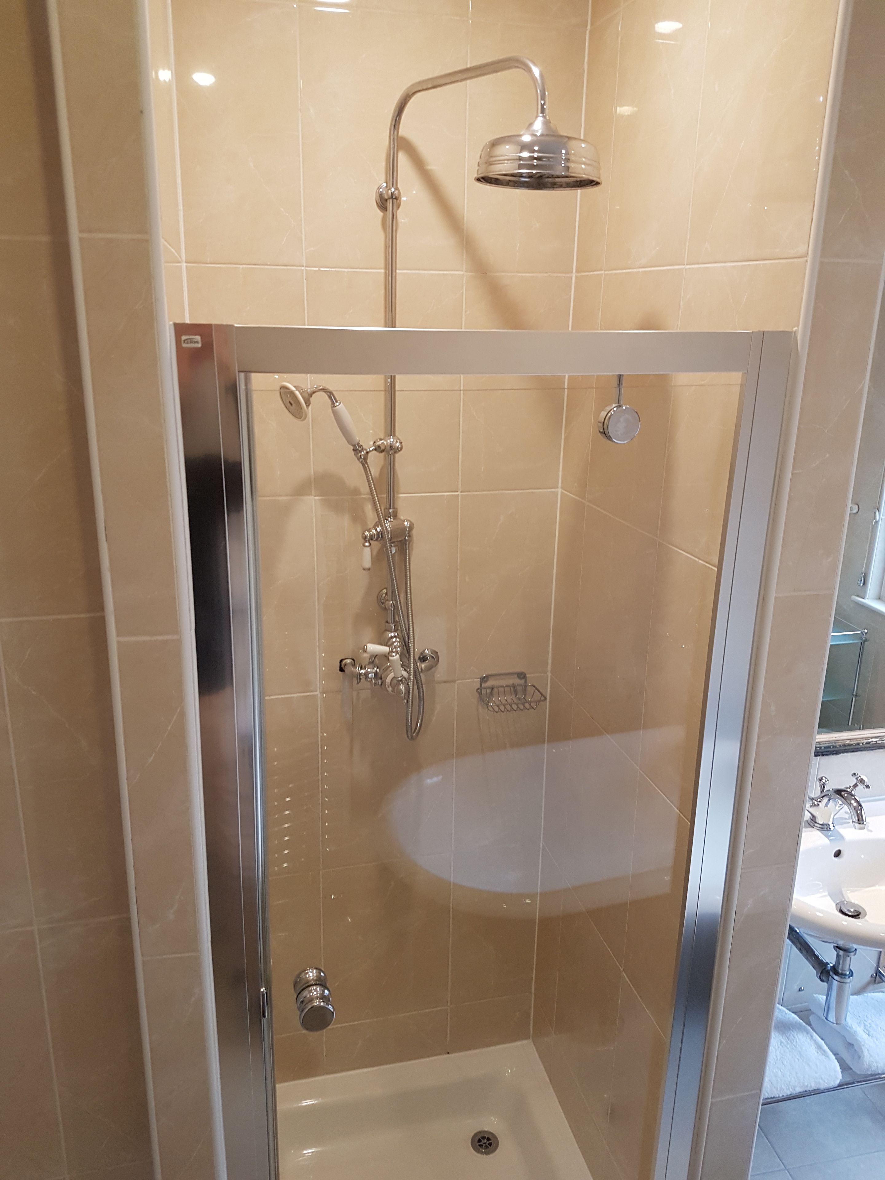 Eine begegnete Duschkabine mit Handbrause und am Wand montierter Armatur.