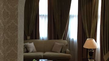 Una sala de estar con sofá, mesa de centro, lámpara y vistas a través de ventanas grandes con cortinas.