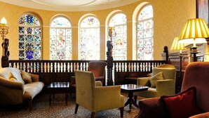 A room with a wooden bench, armchairs, and a table. There are stained glass windows and a lamp. - Quebecs (Leeds)