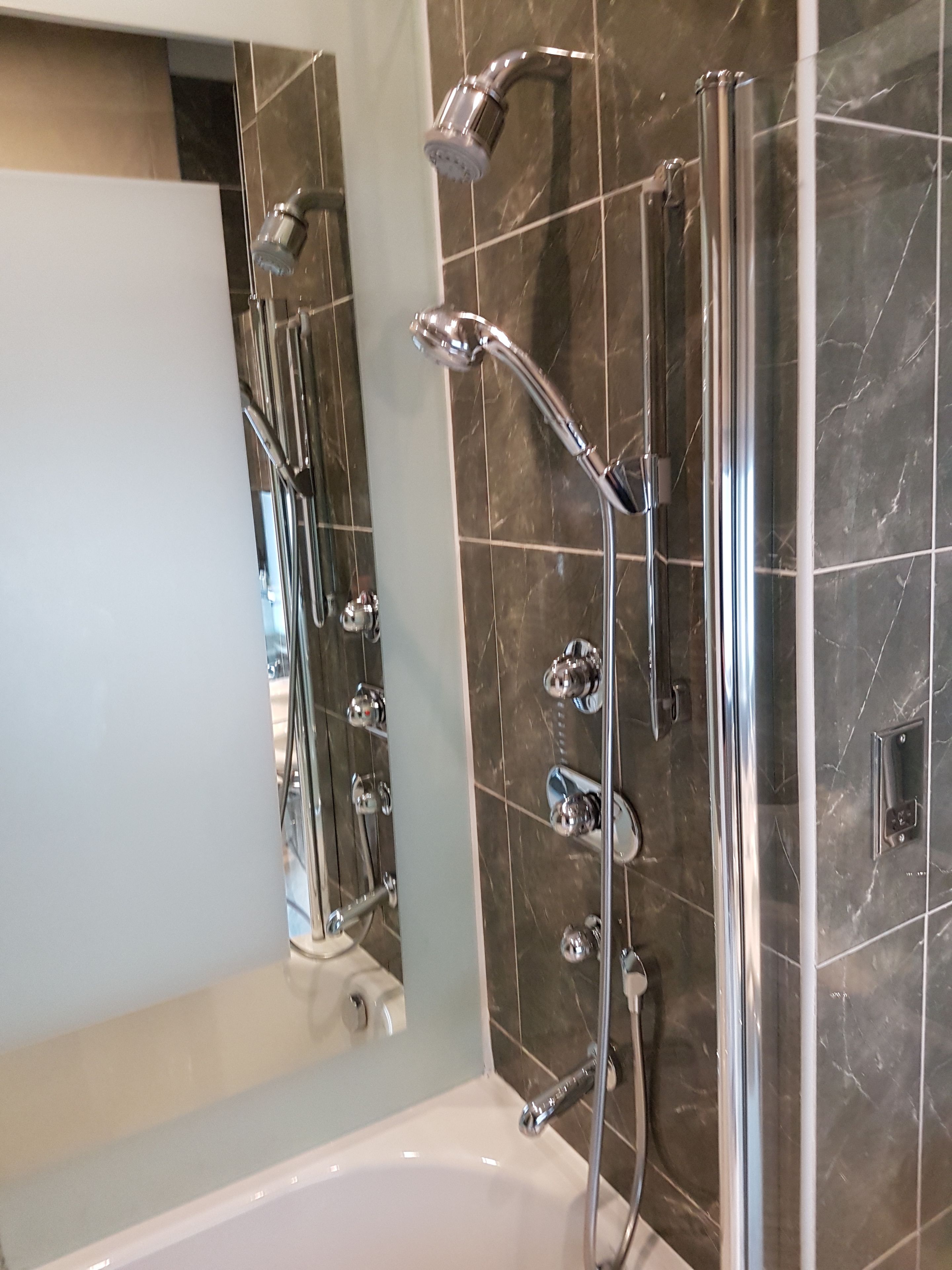 Un baño moderno con una bañera, una ducha con cabezal de ducha manual y un box de ducha con mampara de vidrio.