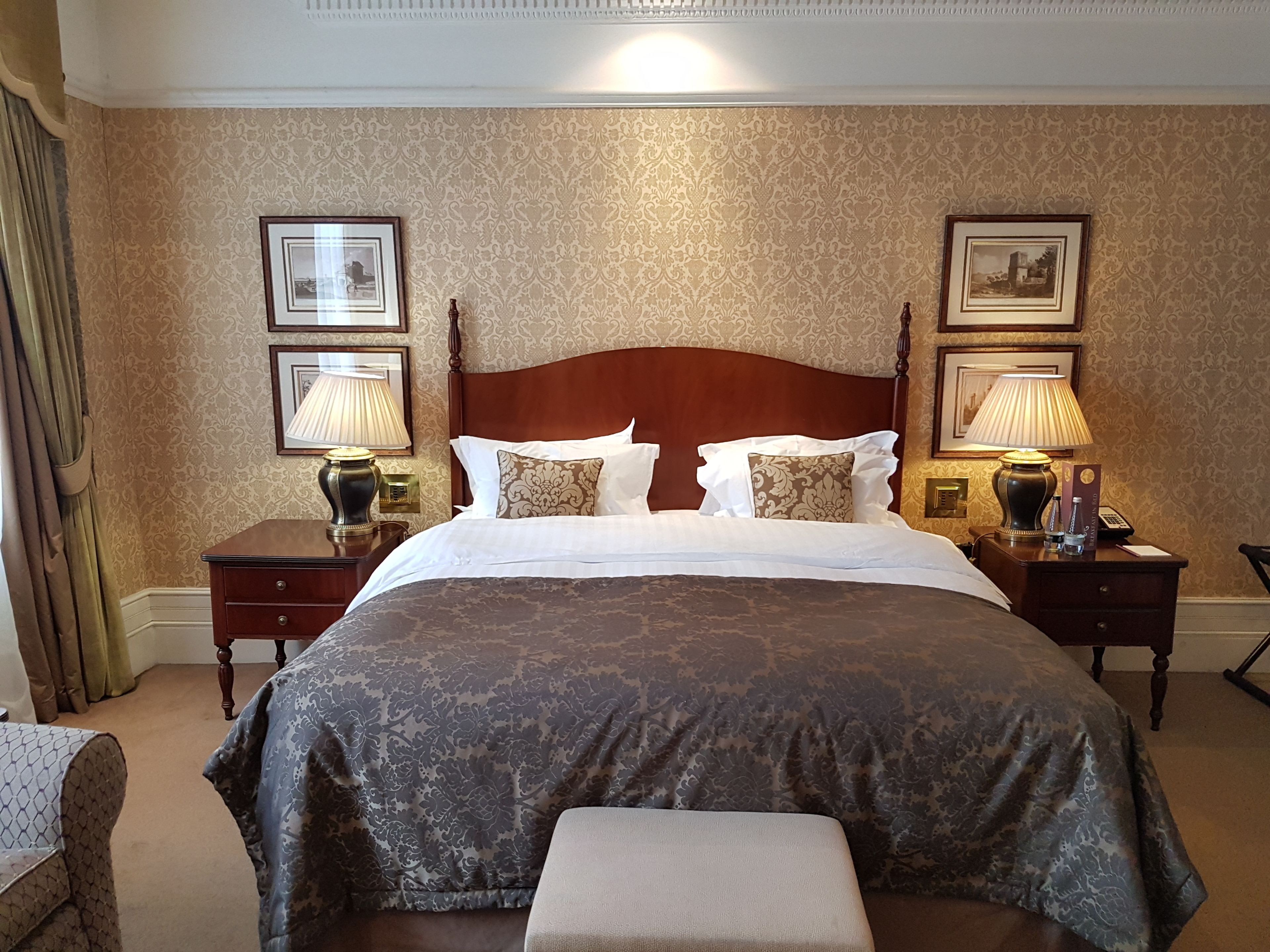 Habitación de hotel con una cama grande, dos mesitas de noche, un cabecero de madera y cuadros enmarcados en las paredes.