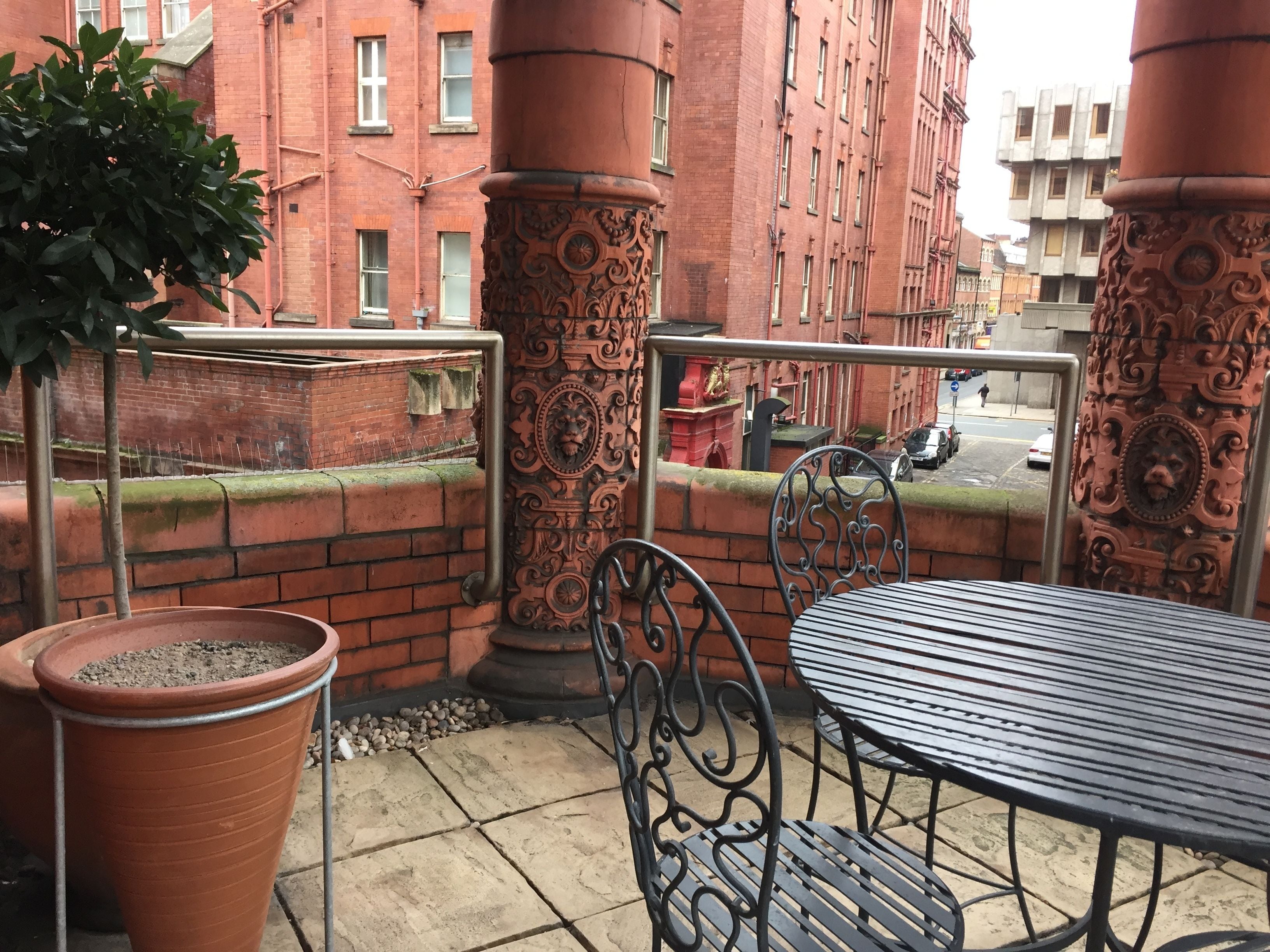 A balcony with a metal table and chairs, terracotta planters, and ornate pillars.