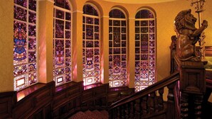 A grand staircase with ornate railings and a lion statue, leading to a room with large stained glass windows. - Quebecs (Leeds)