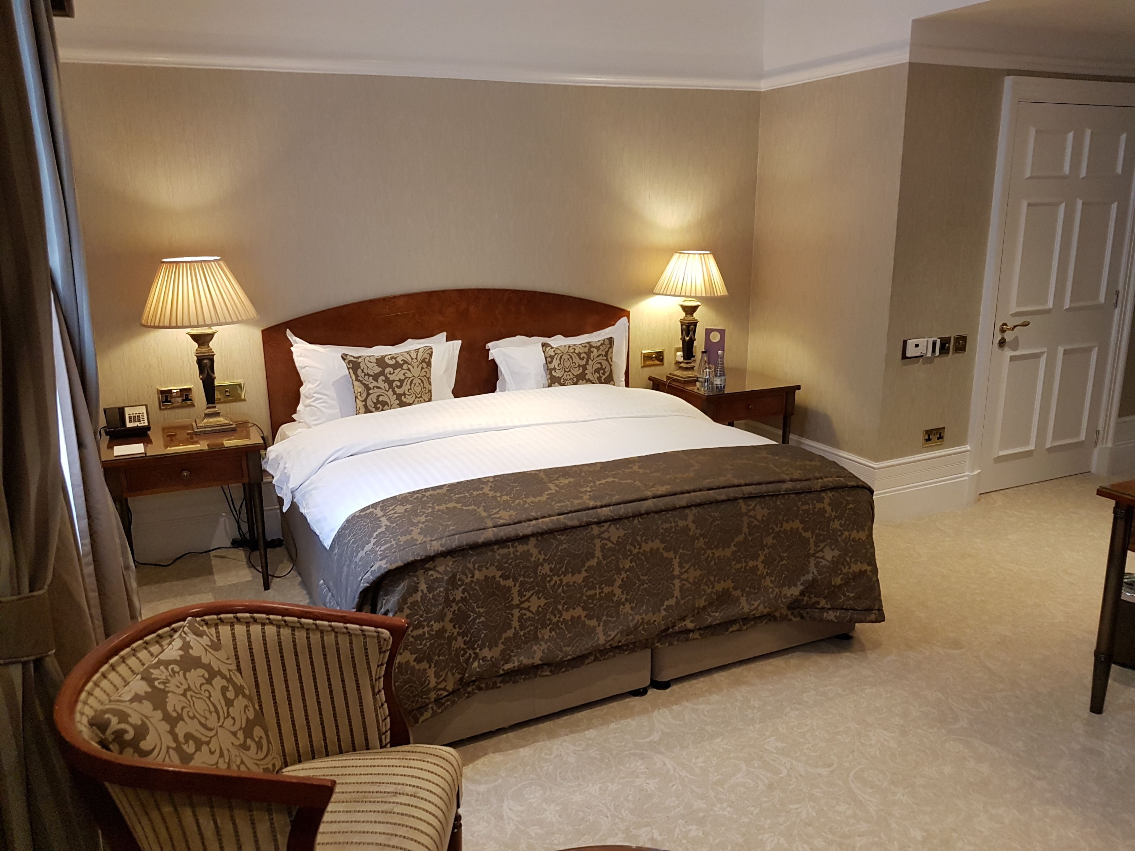A hotel room with a large bed, two bedside tables, a chair, and a door.