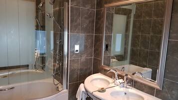 Un baño moderno con ducha envuelta en vidrio, una bañera independiente y un tocador con dos lavamanos.