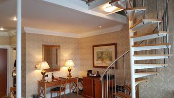 A room with a spiral staircase, a desk with two lamps, a chair, and a framed picture on the wall.