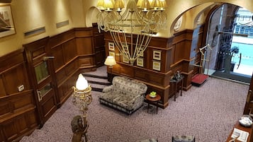 A lobby with a patterned carpet, a sofa, a chandelier, and a statue.